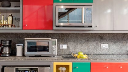 Cocina moderna con gabinetes de colores, microondas, tostadora y frutas en la encimera.